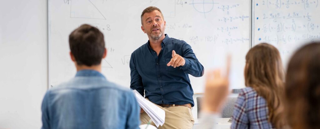 male teacher standing at the front of the class addresses the students