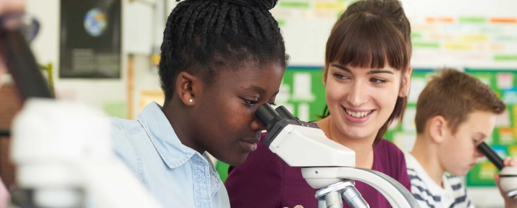 teacher helping student as they look through a microscope