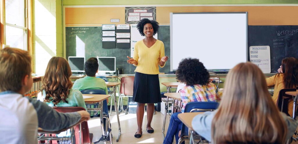 teacher standing at the front of the classroom talking to her students.