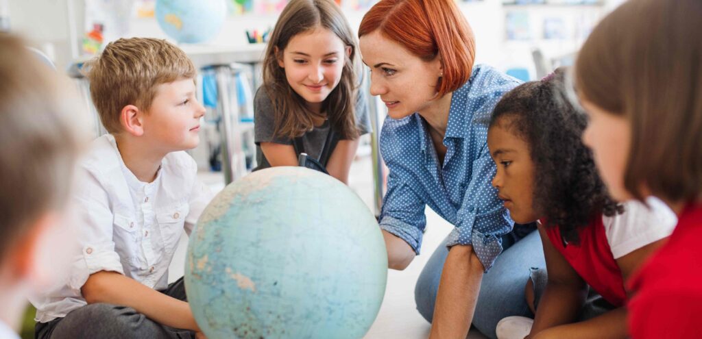 teacher teaching kids while pointing to a globe