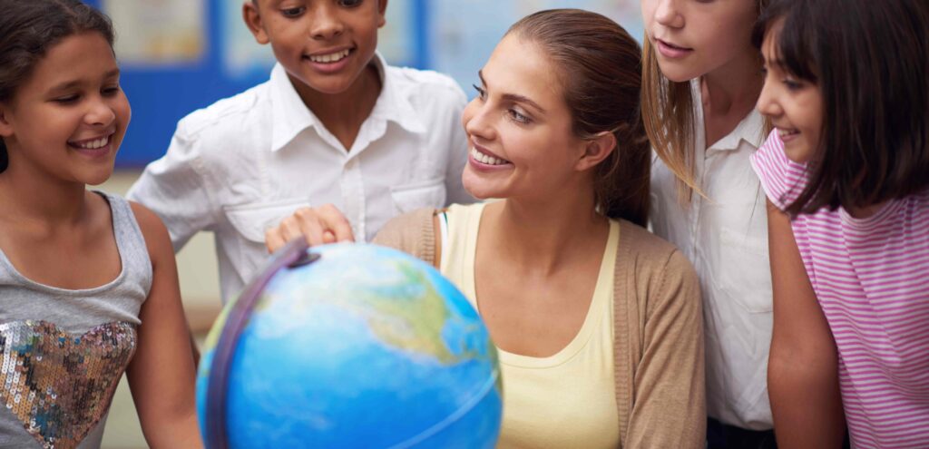 teacher pointing to a globe with a group of students are her